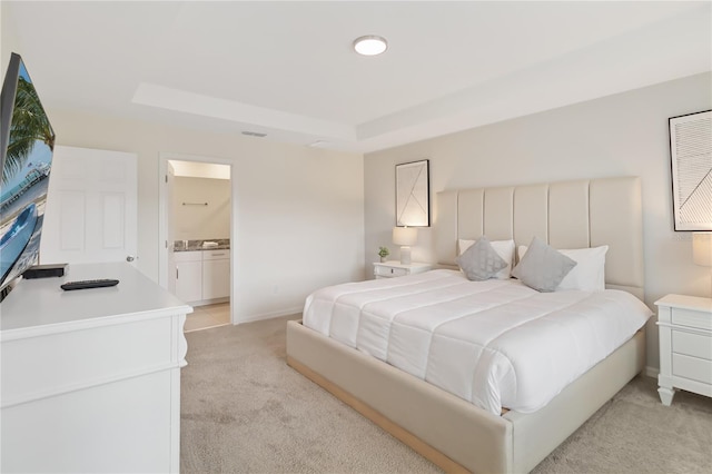 bedroom featuring connected bathroom, light colored carpet, and a raised ceiling