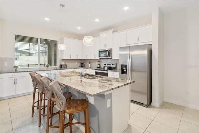 kitchen featuring stainless steel appliances, a center island with sink, sink, pendant lighting, and decorative backsplash