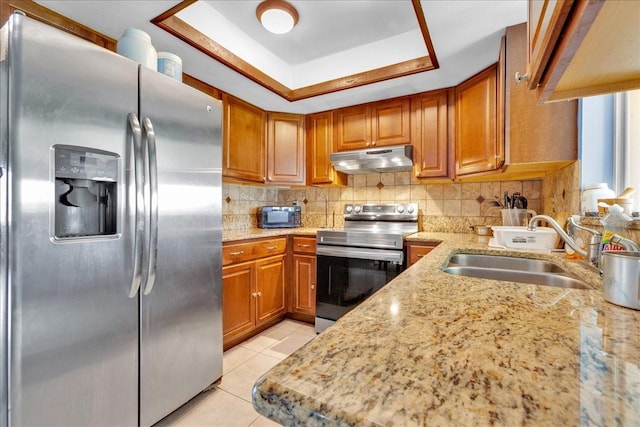 kitchen with sink, a raised ceiling, stainless steel appliances, light stone countertops, and decorative backsplash