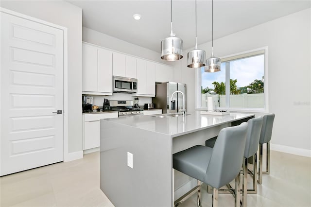 kitchen featuring a kitchen island with sink, a sink, appliances with stainless steel finishes, a breakfast bar area, and white cabinets