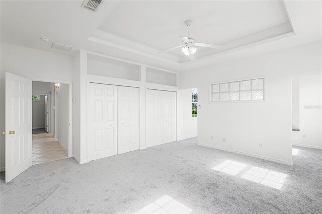 unfurnished bedroom featuring a tray ceiling, ceiling fan, light colored carpet, and two closets