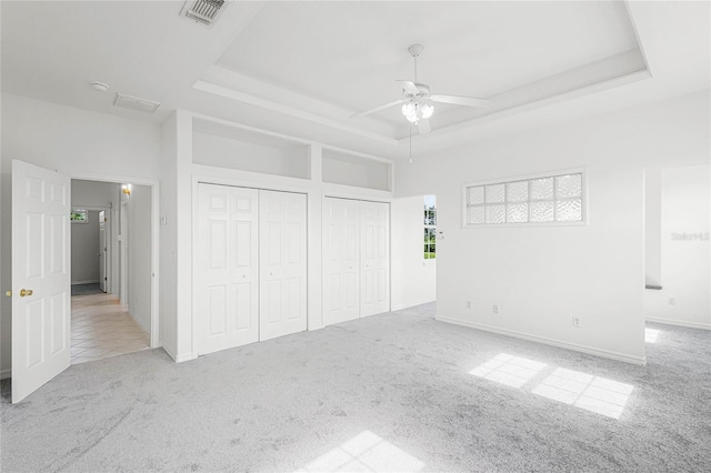 unfurnished bedroom featuring light carpet, two closets, a raised ceiling, and ceiling fan