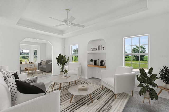 living room with a raised ceiling, built in features, and ceiling fan