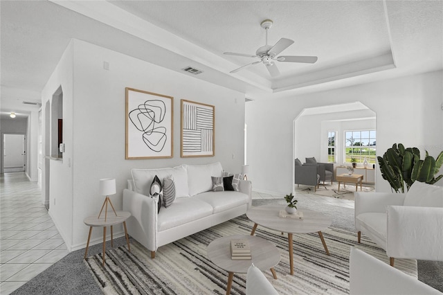 living room with ceiling fan, light tile patterned flooring, a textured ceiling, and a tray ceiling