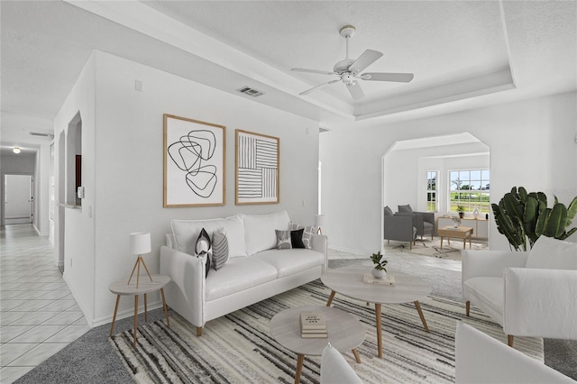 living room featuring a raised ceiling, light tile patterned floors, and ceiling fan