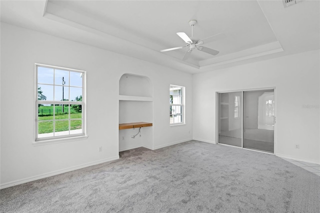 interior space featuring a tray ceiling, built in shelves, ceiling fan, and light carpet