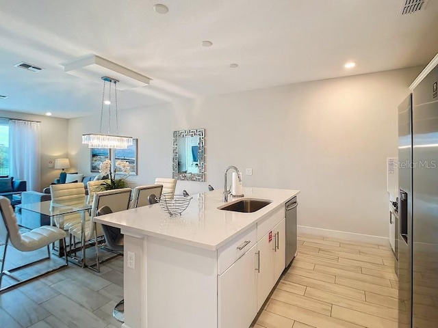 kitchen with sink, appliances with stainless steel finishes, white cabinetry, hanging light fixtures, and a center island with sink