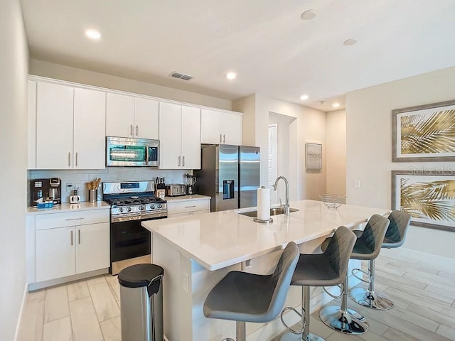 kitchen featuring white cabinetry, appliances with stainless steel finishes, a kitchen island with sink, and decorative backsplash