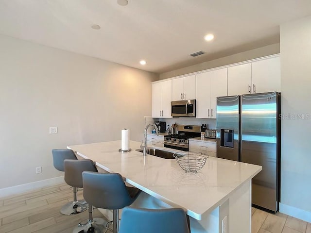 kitchen with stainless steel appliances, a breakfast bar area, a center island with sink, and white cabinets