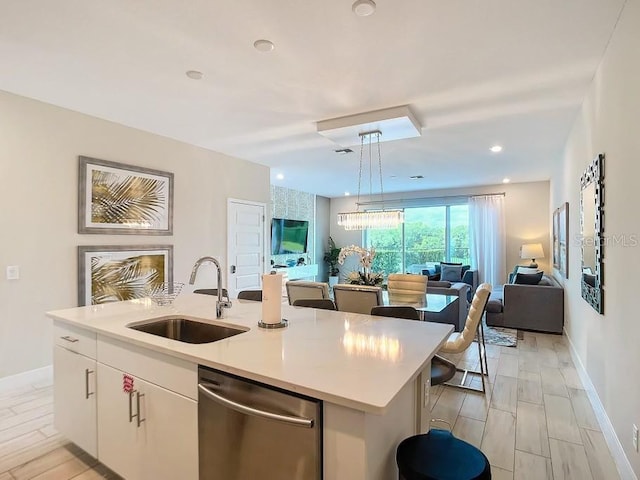 kitchen featuring sink, dishwasher, white cabinetry, hanging light fixtures, and an island with sink