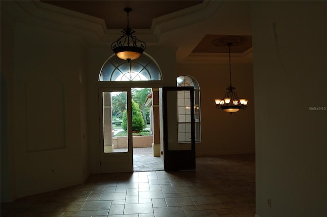 foyer entrance featuring crown molding, a towering ceiling, french doors, a raised ceiling, and a chandelier