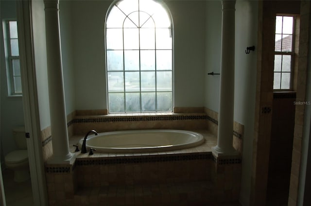 bathroom featuring a relaxing tiled tub, plenty of natural light, and toilet