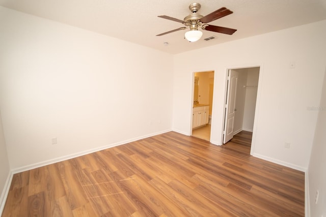 unfurnished bedroom featuring a spacious closet, a closet, connected bathroom, light hardwood / wood-style floors, and ceiling fan