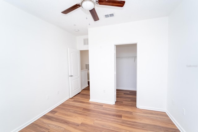 unfurnished bedroom featuring hardwood / wood-style flooring, a spacious closet, a closet, and ceiling fan