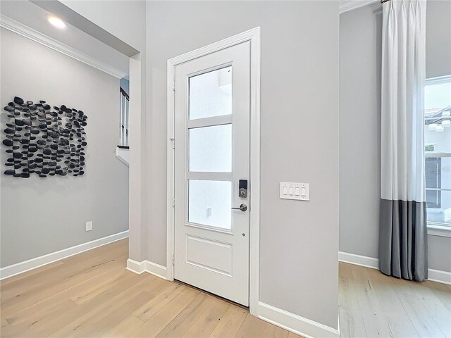 entryway with light hardwood / wood-style floors, crown molding, and a healthy amount of sunlight