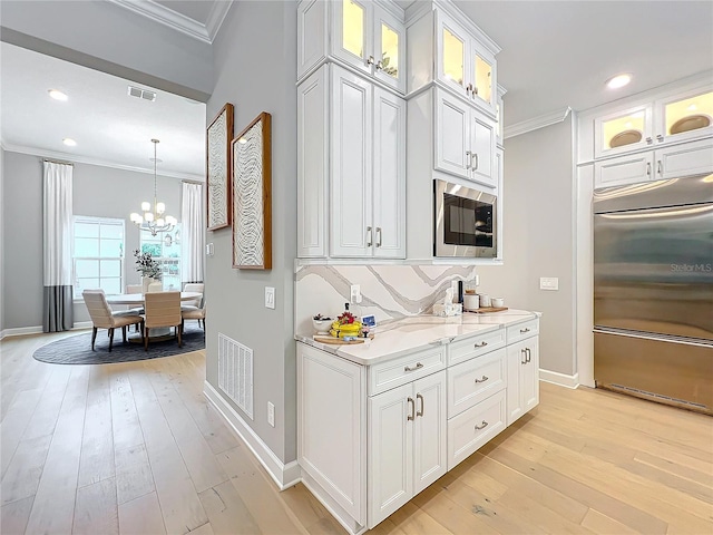 kitchen with light hardwood / wood-style floors, white cabinets, built in appliances, and ornamental molding