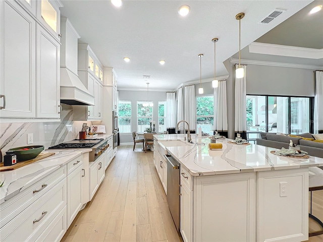 kitchen with appliances with stainless steel finishes, white cabinets, decorative light fixtures, and a center island with sink