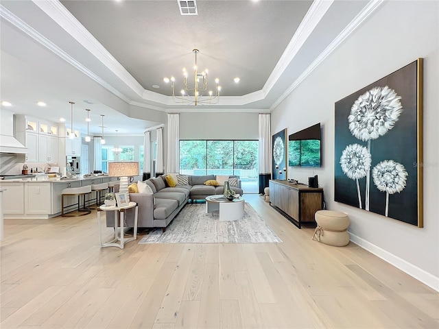 living room featuring light hardwood / wood-style floors, a notable chandelier, ornamental molding, and a tray ceiling