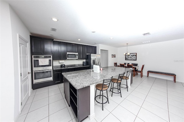 kitchen featuring a center island with sink, stainless steel appliances, a kitchen breakfast bar, light stone counters, and light tile patterned flooring