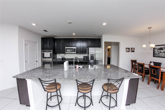 kitchen with sink, stone countertops, light tile patterned floors, appliances with stainless steel finishes, and a kitchen island with sink