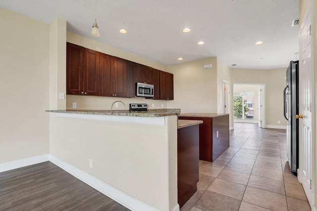 kitchen with appliances with stainless steel finishes, pendant lighting, light stone counters, and kitchen peninsula