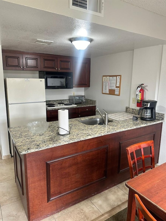 kitchen featuring white refrigerator, light stone countertops, sink, and a textured ceiling