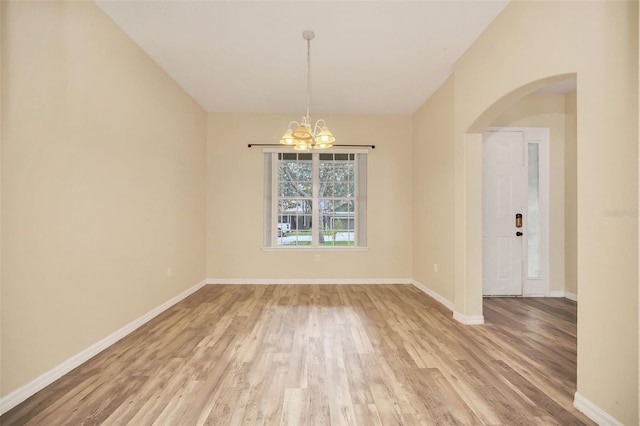 spare room with a notable chandelier and light wood-type flooring