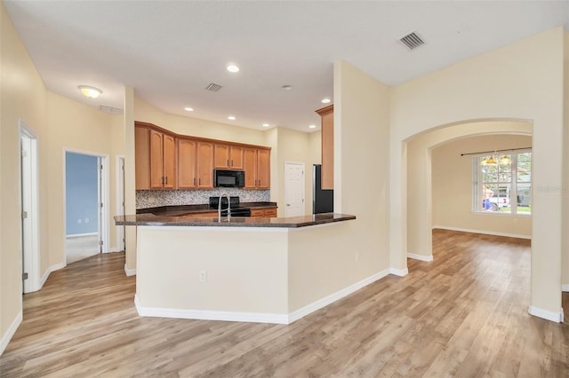 kitchen featuring tasteful backsplash, black appliances, dark stone countertops, kitchen peninsula, and light hardwood / wood-style flooring