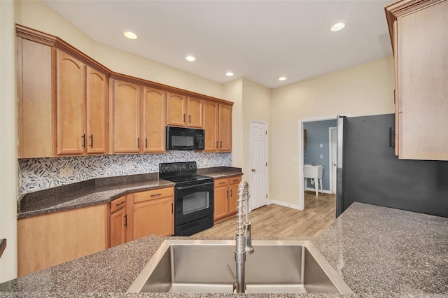 kitchen with sink, backsplash, black appliances, dark stone counters, and light wood-type flooring