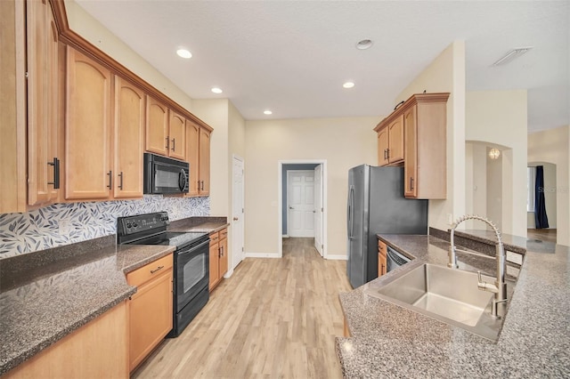 kitchen featuring sink, backsplash, dark stone counters, black appliances, and light hardwood / wood-style flooring