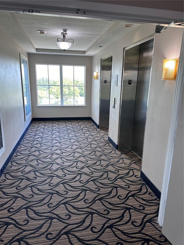 hallway with elevator, carpet, a textured ceiling, and a raised ceiling