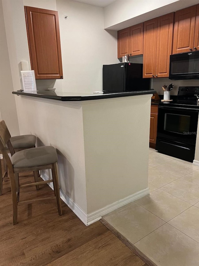 kitchen featuring kitchen peninsula, light hardwood / wood-style flooring, and black appliances