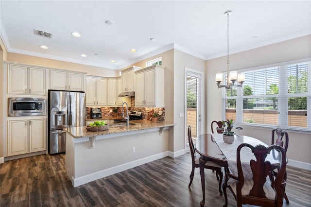 kitchen with sink, hanging light fixtures, stainless steel appliances, cream cabinets, and light stone countertops