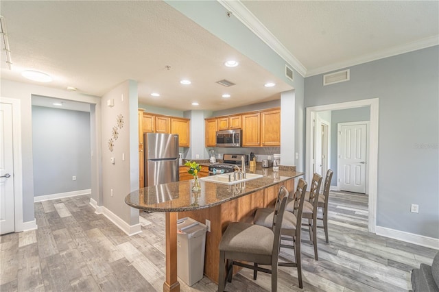 kitchen featuring ornamental molding, appliances with stainless steel finishes, a kitchen breakfast bar, kitchen peninsula, and dark stone counters