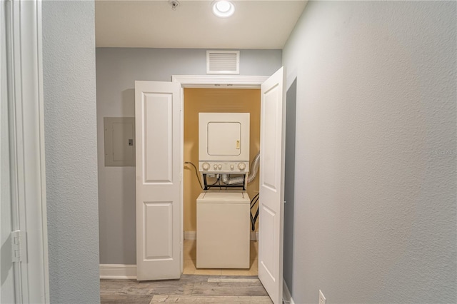 laundry area with stacked washer and clothes dryer, electric panel, and light hardwood / wood-style floors