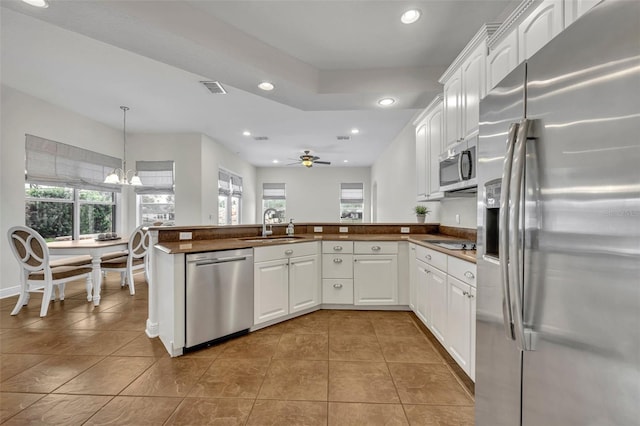 kitchen featuring white cabinets, appliances with stainless steel finishes, kitchen peninsula, and decorative light fixtures