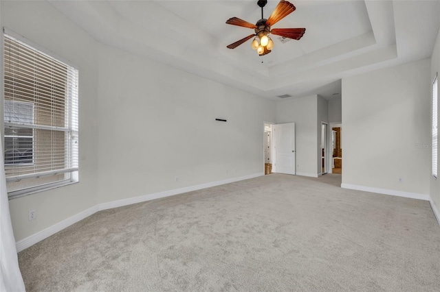 unfurnished room with ceiling fan, a raised ceiling, and light carpet