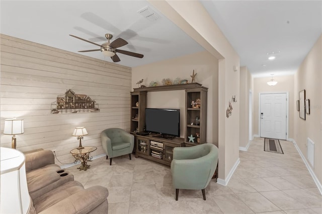 living room featuring ceiling fan, wooden walls, and light tile patterned floors