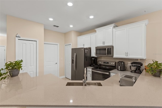 kitchen with sink, appliances with stainless steel finishes, white cabinetry, tasteful backsplash, and kitchen peninsula