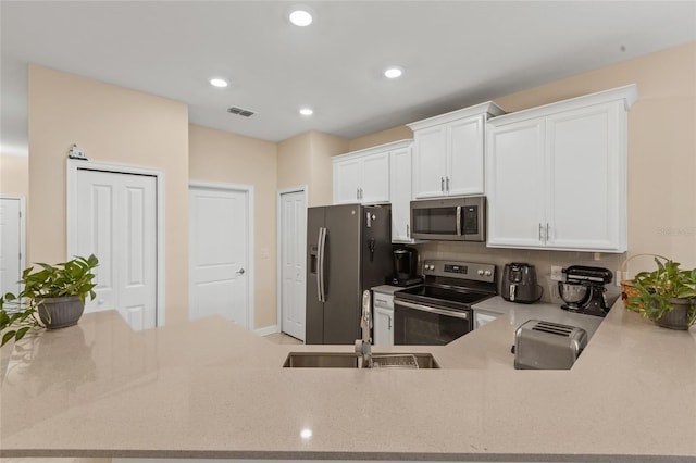 kitchen with visible vents, white cabinets, light stone counters, a sink, and stainless steel appliances