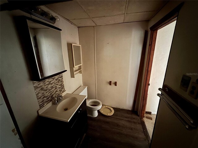 bathroom featuring a drop ceiling, toilet, vanity, decorative backsplash, and hardwood / wood-style flooring