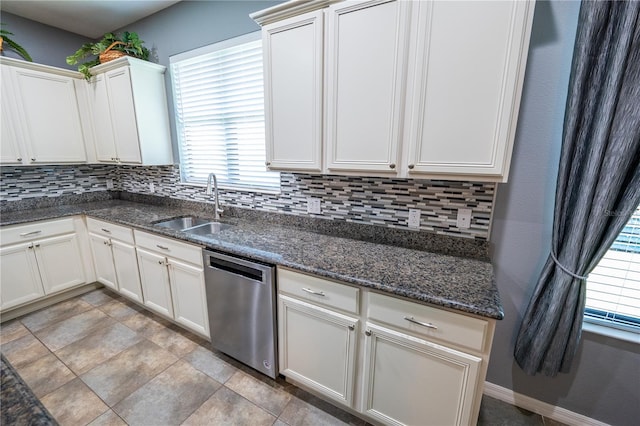 kitchen featuring tasteful backsplash, stainless steel dishwasher, sink, dark stone countertops, and white cabinets