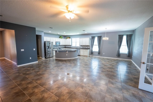 kitchen with appliances with stainless steel finishes, tasteful backsplash, hanging light fixtures, white cabinets, and a kitchen island