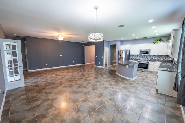 kitchen featuring appliances with stainless steel finishes, a kitchen island, white cabinetry, backsplash, and hanging light fixtures