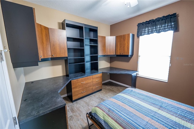 bedroom featuring built in desk, ceiling fan, light hardwood / wood-style flooring, and multiple windows