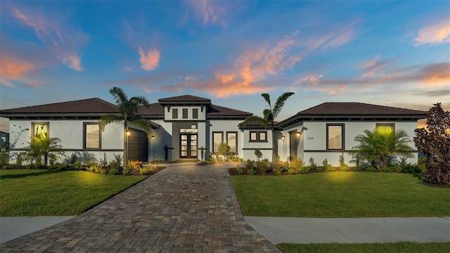 view of front of home featuring stucco siding, french doors, decorative driveway, and a yard