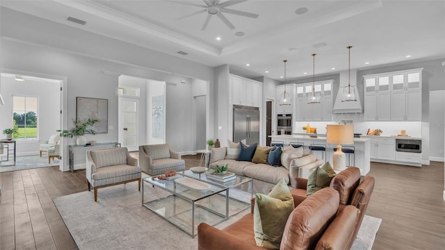 living room with ceiling fan, ornamental molding, light wood-type flooring, and a raised ceiling