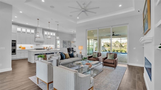 living room with ceiling fan, a raised ceiling, sink, hardwood / wood-style flooring, and crown molding