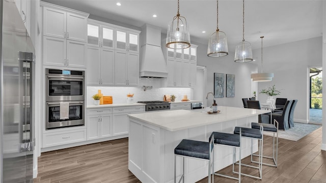 kitchen with pendant lighting, stainless steel appliances, an island with sink, and white cabinets