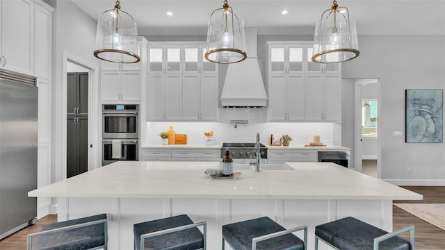 kitchen featuring hanging light fixtures, an island with sink, stainless steel appliances, and white cabinets